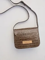 Cartera tipo mini bag de cuero con textura de reptil, color marrón, con solapa frontal y correa larga ajustable para usar al hombro o cruzada.