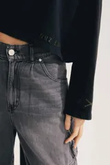 Buzo negro de algodón, con cuello polo y cierre frontal de botones, manga larga y calce oversized cropped. Presenta pequeño estampado tono sobre tono en el ruedo.
