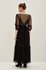 Vestido midi de tul negro con bordados brillantes y pedrería en el escote. Presenta mangas abullonadas, corte imperio y falda con volado en el ruedo. Incluye viso interior.