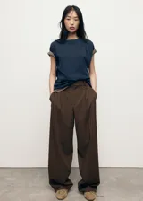 Pantalón de vestir marrón de tiro bajo y diseño wide leg, con pinzas frontales, trabillas para cinturón, bolsillos laterales y cierre oculto con botón, gancho y cremallera.