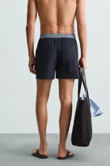 Bañador de hombre azul marino con cintura elástica gris y cordón ajustable. Presenta un pequeño texto estampado en relieve en la parte inferior izquierda.