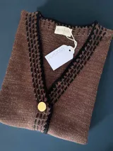 Chaleco tejido color tostado con destellos de lurex, escote en V y cierre frontal con botones. Presenta detalles de bordados y terminaciones en crochet en color crudo.