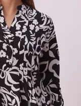 Blusa de gasa estampada con diseño geométrico multicolor, cuello a la base con escote en V y abertura frontal con botones. Presenta detalle de plisado en la parte delantera y mangas largas con sistema de ajuste mediante presilla y botón.