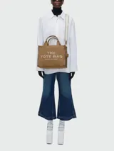 Bolso tote Marc Jacobs modelo The Jacquard, confeccionado en tejido de lona negro con detalles en blanco. Presenta el logo de la marca y la inscripción 'THE TOTE BAG' en el frente, con doble asa superior y correa ajustable extraíble.