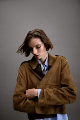 Chaqueta corta de efecto ante en color marrón, con cuello solapa, manga larga y trabillas en los hombros. Presenta cierre frontal con botones y bolsillos delanteros de doble vivo.