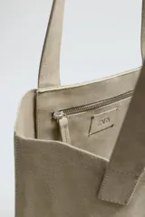 Bolso tipo shopper fabricado en cuero con acabado serraje color gris oscuro. Compartimento principal sin cierre con bolsillo interior con cremallera. Dos asas de mano fabricadas en cuero.