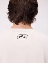 Buzo de cuello redondo Rusty, confeccionado en tejido de algodón y poliéster, con diseño liso en color beige, puños y ruedo acanalados, y detalle de etiqueta de la marca en el frente.