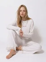 Pijama de algodón color crema, compuesto por una remera de manga larga con bordado delicado en el pecho y un pantalón largo con terminaciones de encaje en el ruedo y la cintura.