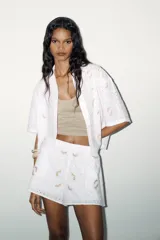 Shorts blancos con cintura elástica, bolsillos laterales ocultos y forro interior. Presenta bordados de flores en tonos rosados y amarillos.