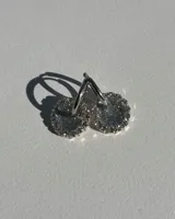 Par de aros de acero quirúrgico con dije circular de resina brillante color plateado, rodeado de strass.