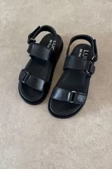 Sandalia plana color marrón de cuero vacuno, con tres tiras ajustables con hebillas y cierre de velcro, y base acolchada.