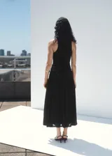 Vestido midi negro sin mangas, con cuello redondo y diseño ajustado en el torso mediante fruncidos laterales, que se abre en una falda evasé fluida.
