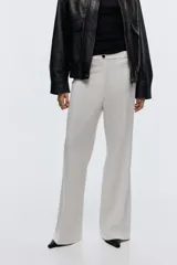 Pantalón sastrero de color blanco, tiro alto, con cierre frontal de botón y piernas acampanadas con pliegues marcados.