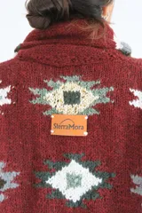 Saco tejido a mano de lana, color bordó con diseño geométrico estampado en tonos gris, blanco y verde. Presenta cuello solapa, cierre frontal con botones grandes y bolsillos delanteros.