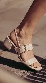 Sandalia de cuero color beige con taco cuadrado de 4 cm, tiras delanteras, tira ajustable con hebilla metálica dorada y tira elástica trasera.