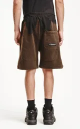 Bermuda de algodón rústico color negro con efecto acid wash/oxidado, corte oversize y cintura elástica. Presenta bolsillos laterales con cierre y un pequeño logo bordado en la parte inferior derecha.