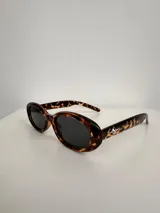 Lentes de sol con armazón ovalado de color negro y cristales tonalidad marrón. Presentan un detalle metálico en forma de estrella en las patillas.