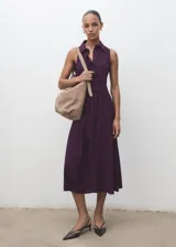 Vestido midi color violeta oscuro, con cuello camisero, sin mangas y cierre frontal con botones. Presenta un corte evasé con cinturón ajustable a la cintura.