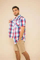 Camisa de manga corta con estampado de cuadros en tonos verdes, azules y blancos. Presenta cuello clásico, cierre frontal con botones y dos bolsillos delanteros con solapa.