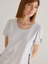 Remera de algodón con cuello redondo y mangas cortas abullonadas. Presenta detalles decorativos de cartera con botones en el lateral del cuerpo y en los puños, combinados con aplicaciones de lino.