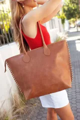 Bolso tote de cuero color tostado con costuras blancas a la vista en los laterales y doble asa de hombro.