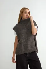 Chaleco de tejido de punto con cuello alto, diseño holgado y textura suave. Presenta un tono marrón jaspeado con terminaciones acanaladas en el ruedo.