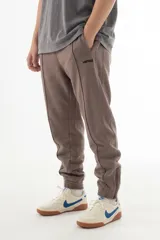 Pantalón de jogging color visón, con corte relajado y costuras frontales marcadas. Presenta cintura elástica, logo bordado en la pierna y cierres en los tobillos para ajustar el calce.