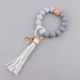 Llavero con pulsera elástica de cuentas redondas de silicona en tonos gris y blanco marmolado, con un cubo de madera natural y una borla de cuero sintético blanca.
