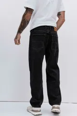 Pantalón de jean corte relaxed, color negro, con diseño de cinco bolsillos y cierre frontal con botón y cremallera.