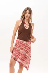 Pollera midi de corte asimétrico con tejido de crochet y patrón en zigzag multicolor en tonos rojo, rosado y beige.