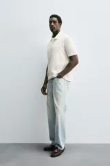 Polo de hombre color blanco hueso, de corte regular fit, con cuello solapa y tapeta de dos botones. Manga corta terminada en rib.