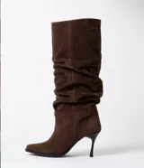 Bota de caña alta confeccionada en gamuza color marrón, con diseño slouchy de efecto arrugado y tacón fino de altura media.
