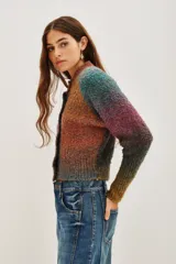 Cardigan de punto con diseño multicolor en tonos tierra y violeta, de corte cropped y manga larga. Presenta cierre frontal con botones oscuros y cuello redondo.