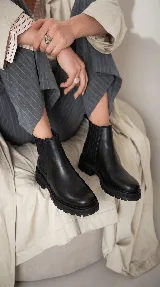 Bota tipo Chelsea de cuero negro con suela track dentada y paneles laterales elásticos.