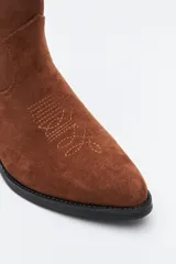 Bota corta estilo western de gamuza color marrón, con taco cuadrado negro y puntera estilizada. Presenta un detalle de estrella aplicada en el lateral y tirador en la parte superior.