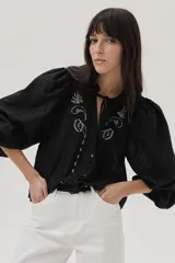 Blusa blanca con lunares en relieve, cuello con volados y lazos, mangas abullonadas 3/4 y bordados con lentejuelas en el frente.