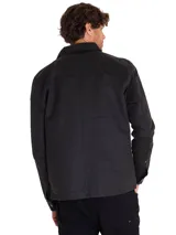 Chaqueta de estilo chore en color negro, confeccionada en sarga encerada. Presenta cierre frontal de cremallera metálica, cuello clásico, bolsillo en el pecho con cierre y etiqueta de la marca Caterpillar.