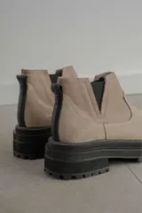 Bota tipo chelsea de punta redonda, confeccionada en una combinación de cuero texturizado y gamuza en tonos marrones. Presenta elásticos laterales negros y una suela track robusta de goma negra.