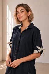 Vestido corto de lino verde militar, con cuello polo, cierre frontal parcial con botones y mangas cortas con detalle de tiras para anudar en los puños.