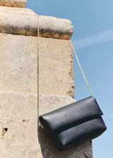 Bolso tipo pochette de efecto piel en color negro, con cierre de solapa y botón magnético. Incluye una fina cadena dorada como asa bandolera.