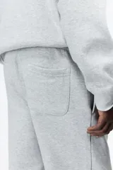 Pantalón de jogging gris claro, de corte relajado, con cintura elástica ajustable con cordón, bolsillos laterales y puños acanalados.