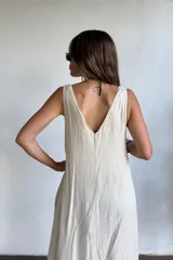 Vestido largo sin mangas, color natural/crudo, con escote en V profundo y corte holgado. Presenta aberturas laterales en la falda.