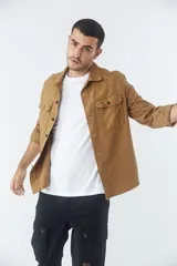 Sobrecamisa de jean color tostado, con cuello clásico, cierre frontal con botones y dos bolsillos frontales con solapa. Presenta mangas largas con puños abotonados y un pequeño parche decorativo en el ruedo.