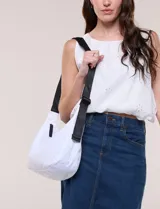 Cartera bandolera de lona blanca con silueta de medialuna, cierre superior negro y correa regulable en contraste.