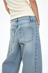 Jean de cinco bolsillos en denim de algodón rígido, con diseño de piernas curvas y volumen, de corte holgado desde la cadera hasta los muslos y ligeramente más ceñido en el bajo. Cintura clásica con cierre de botón y cremallera.