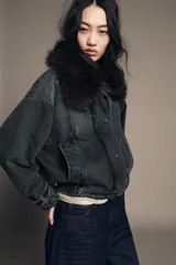 Chaqueta tipo bomber de denim lavado azul, corte holgado, con cuello solapa y aplicación de pelo sintético marrón desmontable. Presenta bolsillos delanteros y bajo acabado en elástico.