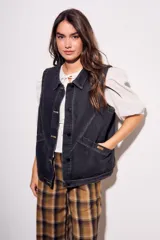 Chaleco oversize de denim negro con costuras en hilo ocre, cuello camisero, cierre frontal con botones y bolsillos delanteros.