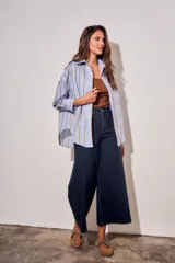 Camisa de corte oversize con estampado de rayas verticales en tonos azul claro y mostaza. Presenta cuello clásico, cierre frontal con botones y mangas largas con puños abotonados.