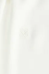 Camisa de manga larga con cuello clásico y botonadura frontal. Presenta una corbata extraíble a juego, puños con cierre de botón y un sutil detalle bordado en el pecho. El diseño incluye un canesú con pliegue en la espalda y un bajo redondeado con aberturas laterales.