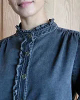 Camisa de jean azul con cuello alto con volados y volados en el frente.